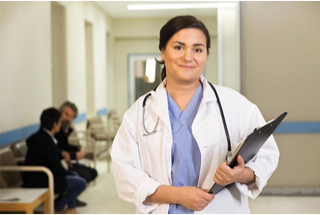 Photograph of a female nurse with brown hair and eyes holding a clipboard and smiling.